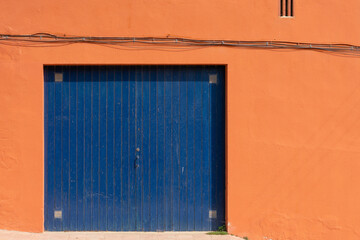 Blue wooden garage door on a terracotta wall. Colorful living background pattern.