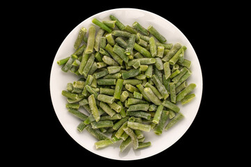 Frozen green beans in white ceramic plate isolated on black background, macro, top view.