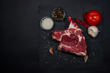 A slice of raw beef meat with spices on a black background.