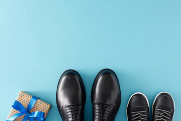 Father's Day celebration concept. Top view flat lay of gift box with ribbon stylish shoes father and child on light blue background with empty space for greeting text or message