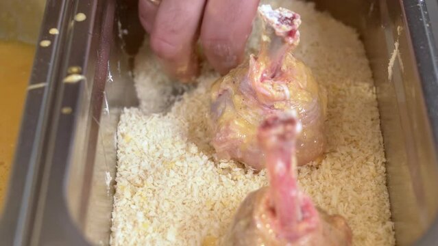 Preparing chicken drumsticks, coating chicken pieces in breadcrumbs.Selective focus, slow motion footage.