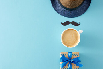 Happy Father's Day concept. Top view flat lay of stylish hat black mustache cup of coffee and gift box on light blue background with empty space for text or greeting message