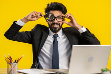 Investigator researcher scientist businessman working at office holding magnifying glass near face looking into camera with big zoomed funny eye, searching, analysing. Professional freelancer man