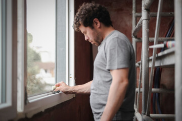 Naklejka premium Caucasian man washes window frame with sponge.