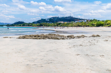 A view past rocky outcrops along the beach towards the town at Tamarindo in Costa Rica in the dry season