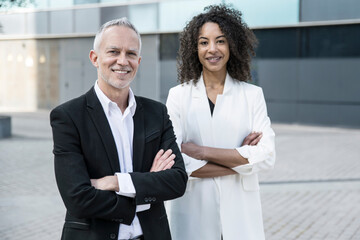 Senior businessman with businesswoman standing outdoors. Two executives with their arms crossed...