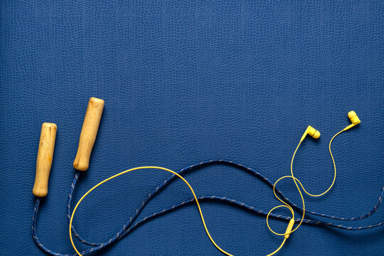 Top view of yellow earphones, jumping rope on the dark blue fitness mat. Empty space