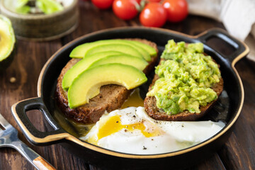 Healthy breakfast, sandwich with avocado and egg. Wholemeal bread toast sliced avocado and poached egg on a rustic table.