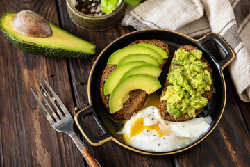 Wholemeal bread toast sliced avocado and poached egg on a rustic table. Healthy breakfast, sandwich with avocado and egg. Copy space.