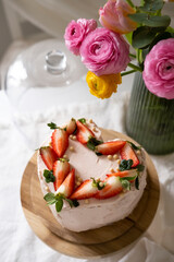 Heart-shaped cake decorated strawberries on a wooden cake stand and pink flowers. Valentine's day dessert
