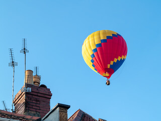 Fototapeta na wymiar Hot air balloon rising above house roof tops clear sky