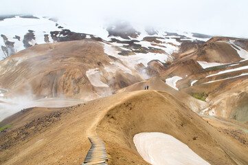 Fototapeta na wymiar 2 people walking in a steaming volcanic rhyolite valley, iceland 