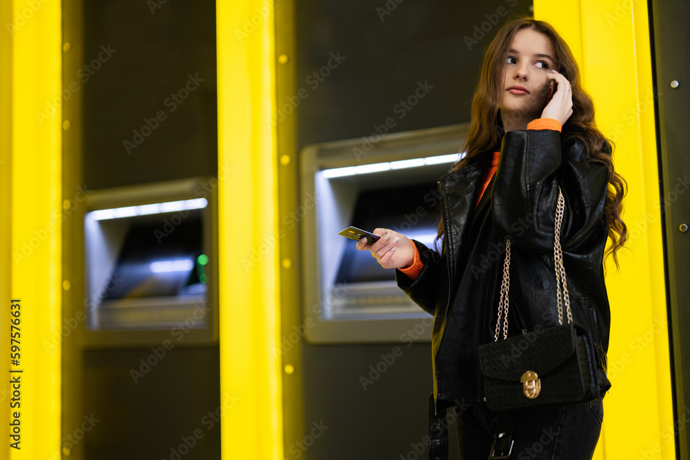 Wall mural young brunette girl withdrawing money from credit card at yellow atm.