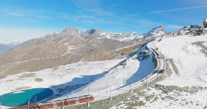 Aerial drone footage of Gornergrat bahn railway climibing up the summit station with Matterhorn mountain peak background in Zermatt on a sunny winter day. Swiss Alps, Switzerland travel journey trip.