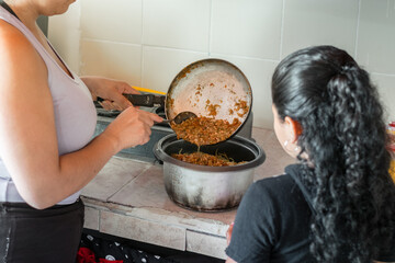 little latin girl learning how her mom pours the stew into the spaghetti. preparing food