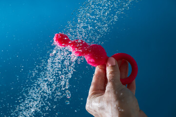 Woman holding pink anal beads under running water on blue background. Sex toy hygiene concept.
