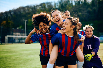 Cheerful female players celebrate scoring goal on soccer match.