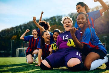 Cheerful goalkeeper and her teammates celebrate winning soccer match at stadium.