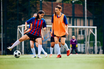Young sportswoman trying to pass her rival during soccer practice on playing field.