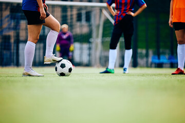 Female soccer player about to kick ball on playing field. - obrazy, fototapety, plakaty