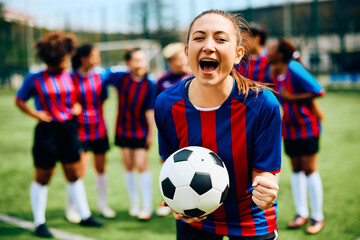 Female soccer player shouts while celebrating at stadium and looking at camera.