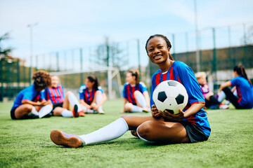 Happy African American female player on soccer training at stadium and looking at camera.