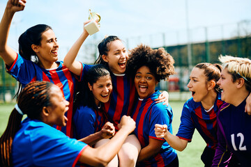 Excited female soccer players have fun while celebrating winning tournament trophy.