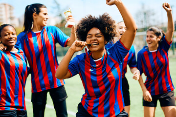 Excited black soccer player biting gold medal after winning championship with her teammates. © Drazen