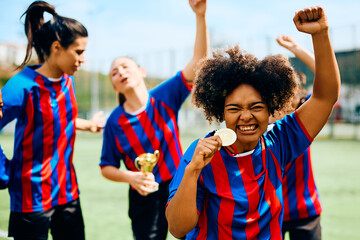 Excited soccer player holds gold medal while celebrating winning championship with her teammates.
