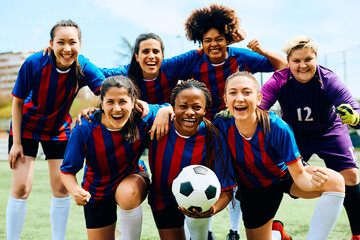Cheerful female soccer players after winning match at stadium looking at camera.
