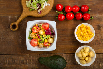 salad with lettuce and cherry tomato with avocado olive oil in a white plate on a wooden table next to all the ingredients.