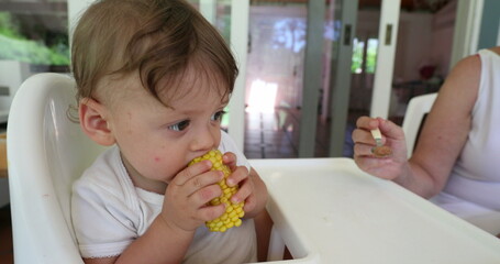Baby eating corn on highchair