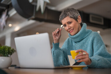 Fototapeta premium One senior woman sitting and drinking coffee while working on laptop casual clothing modern business woman concept 