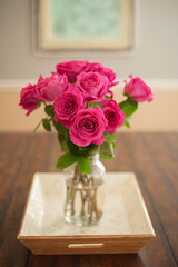 A glass vase of pink roses on a white mother-of-pearl tray placed on a brown wooden table.