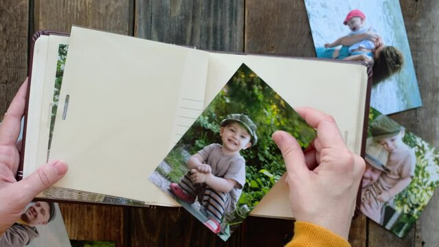 Photo printing concept. Hands adding printed picture of joyful kid to family photo album.