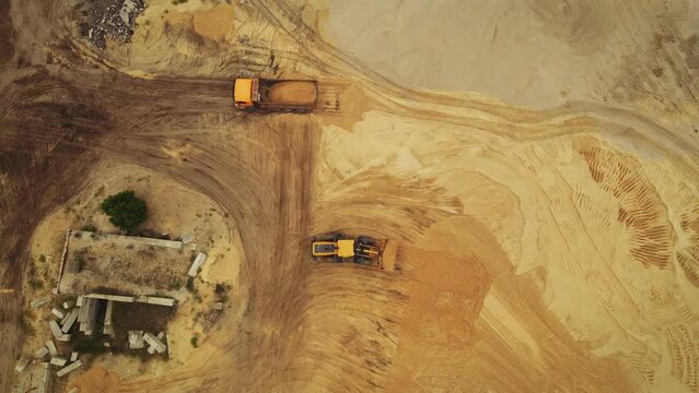 Aerial view of the opencast mine. Front end loader loading sand into dump truck in open pit. Heavy mining machinery working in quarry. Truck transports minerals in opencast