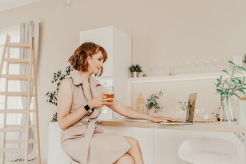 Woman tea macbook kitchen. Portrait of a brunette in a beige dress with a transparent mug in her...