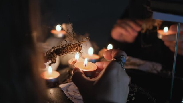 A sorceress or witch performs a rite or a love spell in a dark room with burning candles, close-up