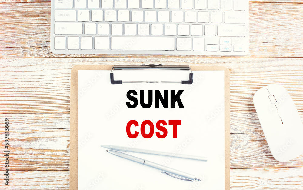 Aufkleber sunk cost text on a clipboard with keyboard on wooden background