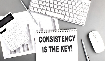 CONSISTENCY IS THE KEY text written on notebook on grey background with chart and keyboard, business concept