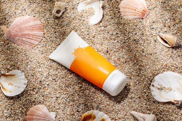 Orange tube of sunscreen on sandy beach top view