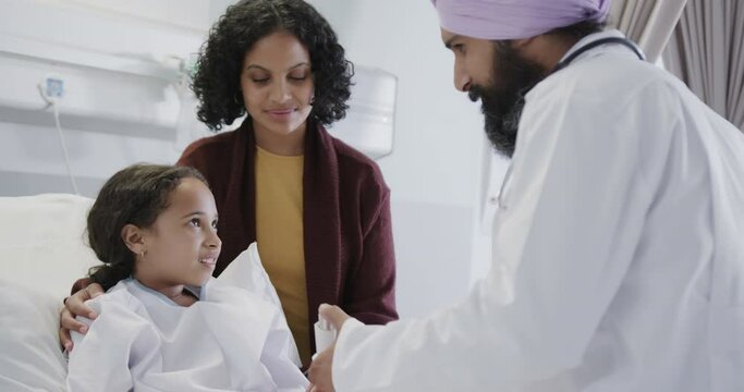 Happy biracial doctor using inhaler on sick girl patient with mother in hospital in slow motion