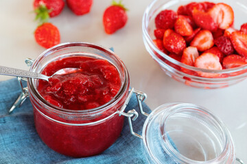 Glass jar with strawberry jam prepared for canning and fresh strawberries in a bowl on the table