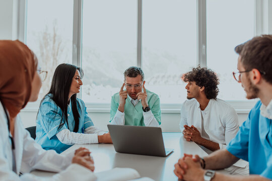 A group of multiethnic medical professionals including doctors, surgeons, and nurses are gathered in a hospital setting discussing patient care and using modern technology to address challenges in