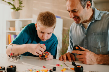 Young boy and his father sitting down at the table and putting together a toy.