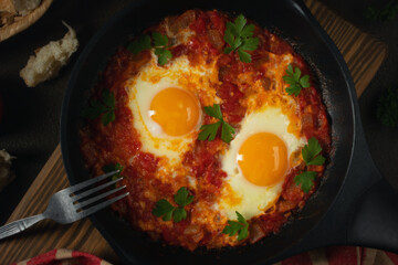 Shakshuka from two eggs in tomato sauce with fresh tomatoes, spices and herbs in a black frying pan. Close-up scrambled eggs