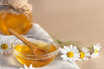 Chamomile syrup in a small bowl and in a jar and chamomile flowers on a linen kitchen towel, copy space