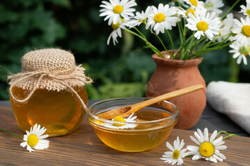 Chamomile syrup in a small bowl and in a jar in the patio on a wooden table