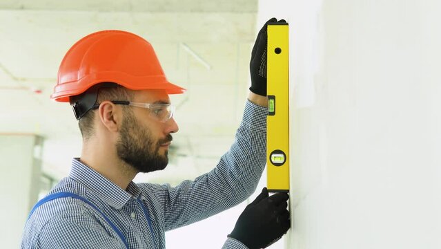 A man builder measures of the vertical deviation of plasterboard wall. Bubble level ruler close up view