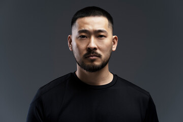 Fototapeta premium Serious, emotional young Asian man standing isolated on gray background, looking at camera